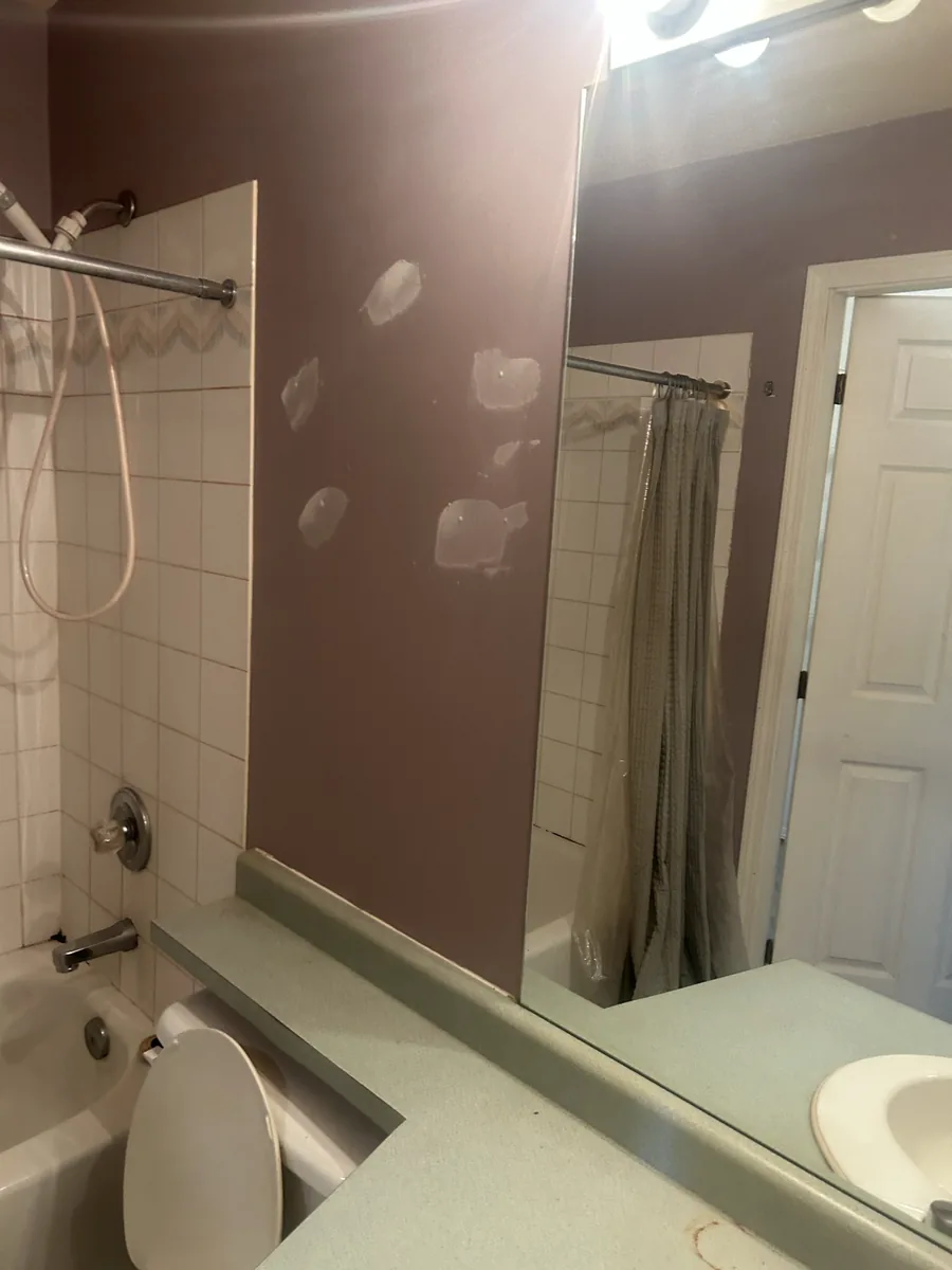 Bathroom with visible wall patches around a tiled tub and a mirrored vanity.