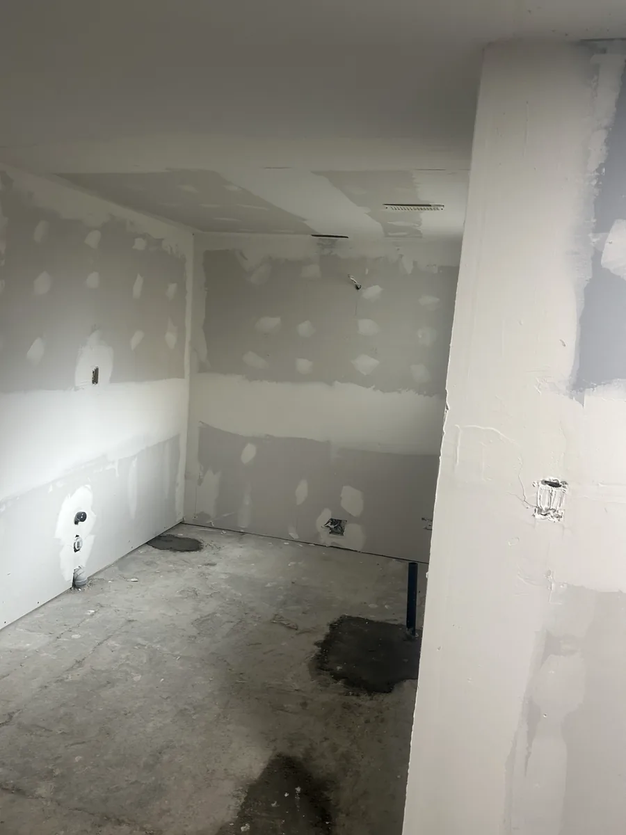 Room with taped drywall, exposed plumbing connections, and an unfinished floor.
